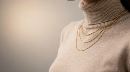 Mujer luciendo un elegante layering de collares de distintas longitudes sobre un jersey de cuello alto, con espacio negativo alrededor