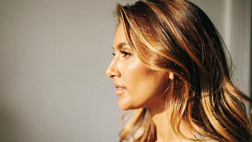 Mujer con cabello castano y reflejos dorados naturales iluminados por luz solar suave, efecto sunkissed