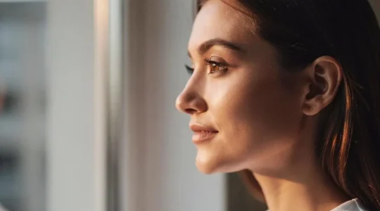 Rostro de mujer con piel luminosa y sana iluminada por luz natural suave, simbolizando la renovación celular equilibrada