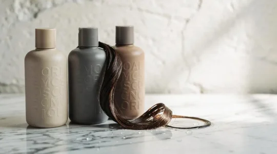 Composición editorial de frascos de champú, acondicionador y mascarilla junto a un mechón de cabello húmedo, representando la elección personalizada del cuidado capilar